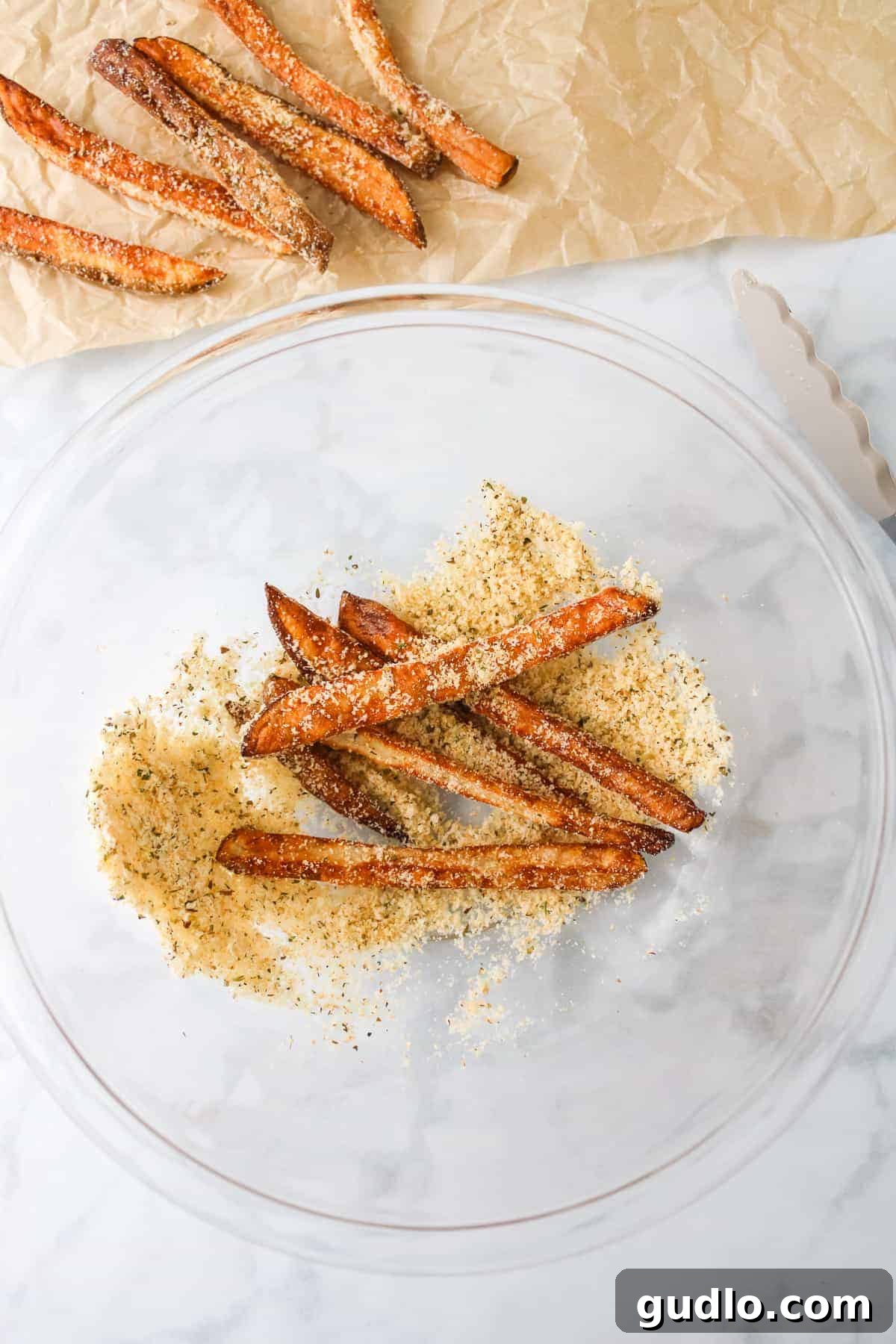 Hot air-fried fries being tossed with grated parmesan cheese, garlic powder, and oregano in a large bowl.