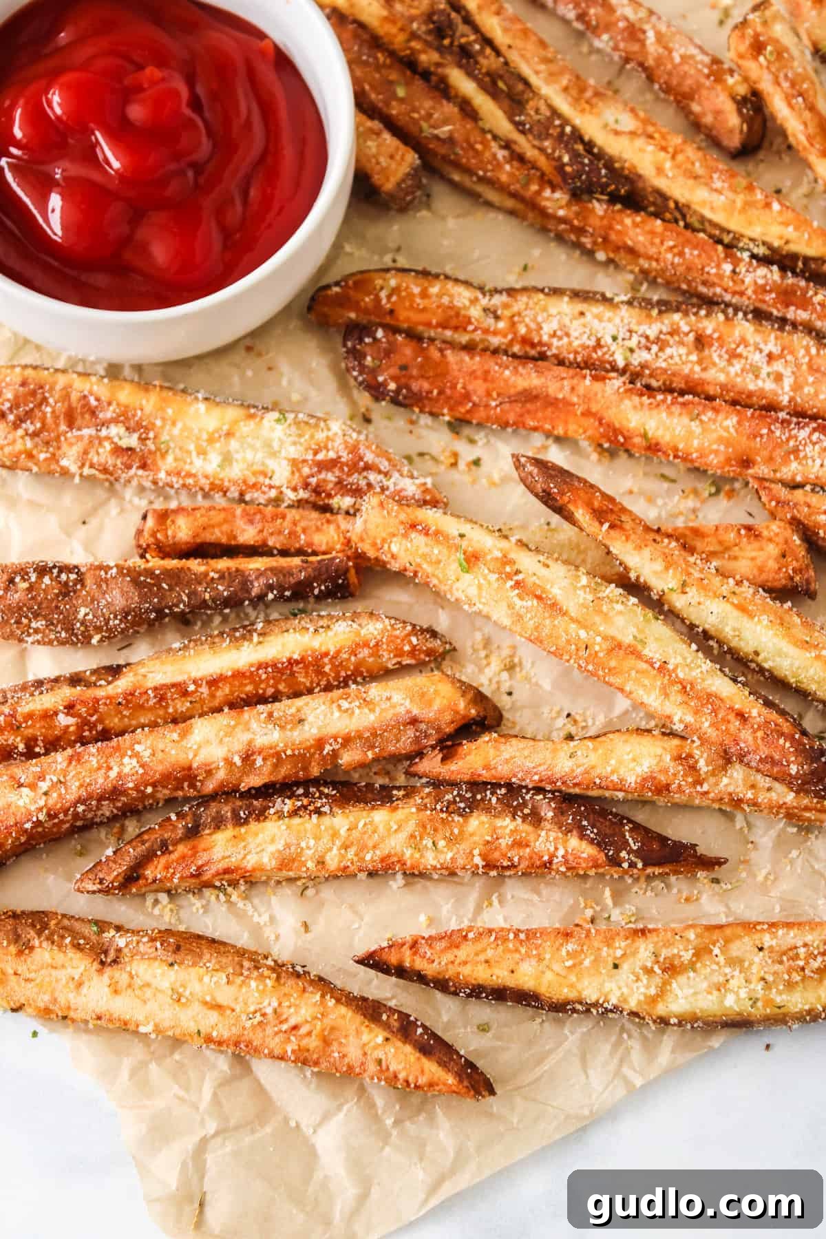 Crispy air fryer garlic parmesan fries served in a paper cone with a side of ketchup, ready to eat.