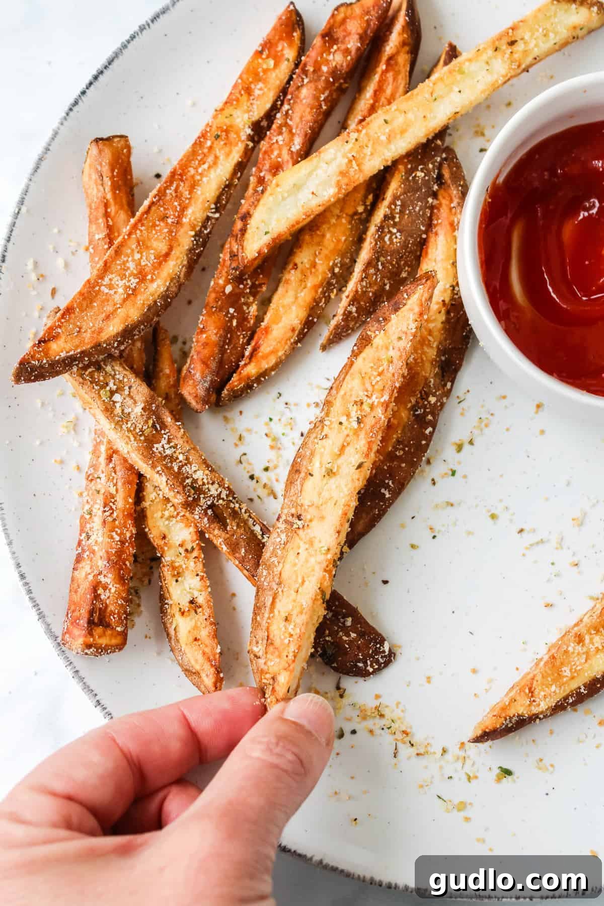 A hand reaching for a crispy garlic parmesan fry from a plate, showcasing the irresistible texture.