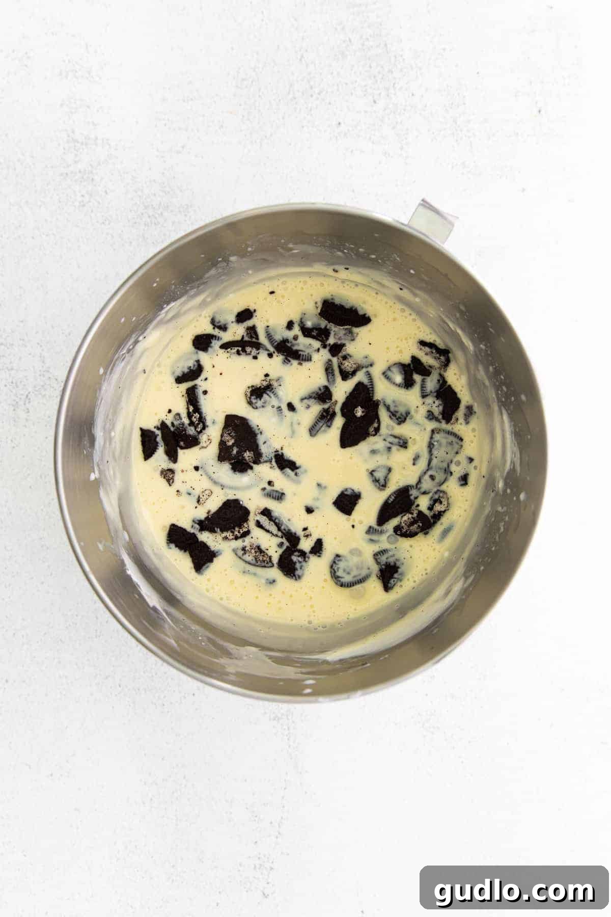 Wet ingredients for Oreo cheesecake filling, including cream cheese and sugar, being mixed in a bowl with a stand mixer.