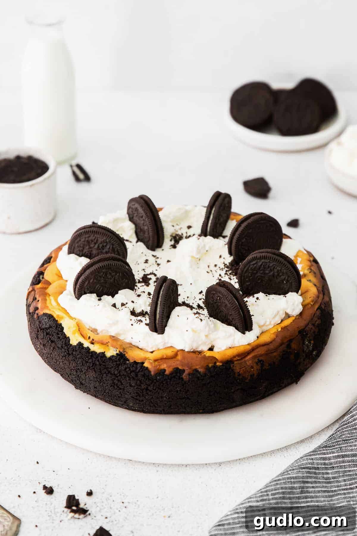 A whole Oreo cheesecake beautifully topped with piped whipped cream and whole Oreo cookies, ready to be sliced and served.