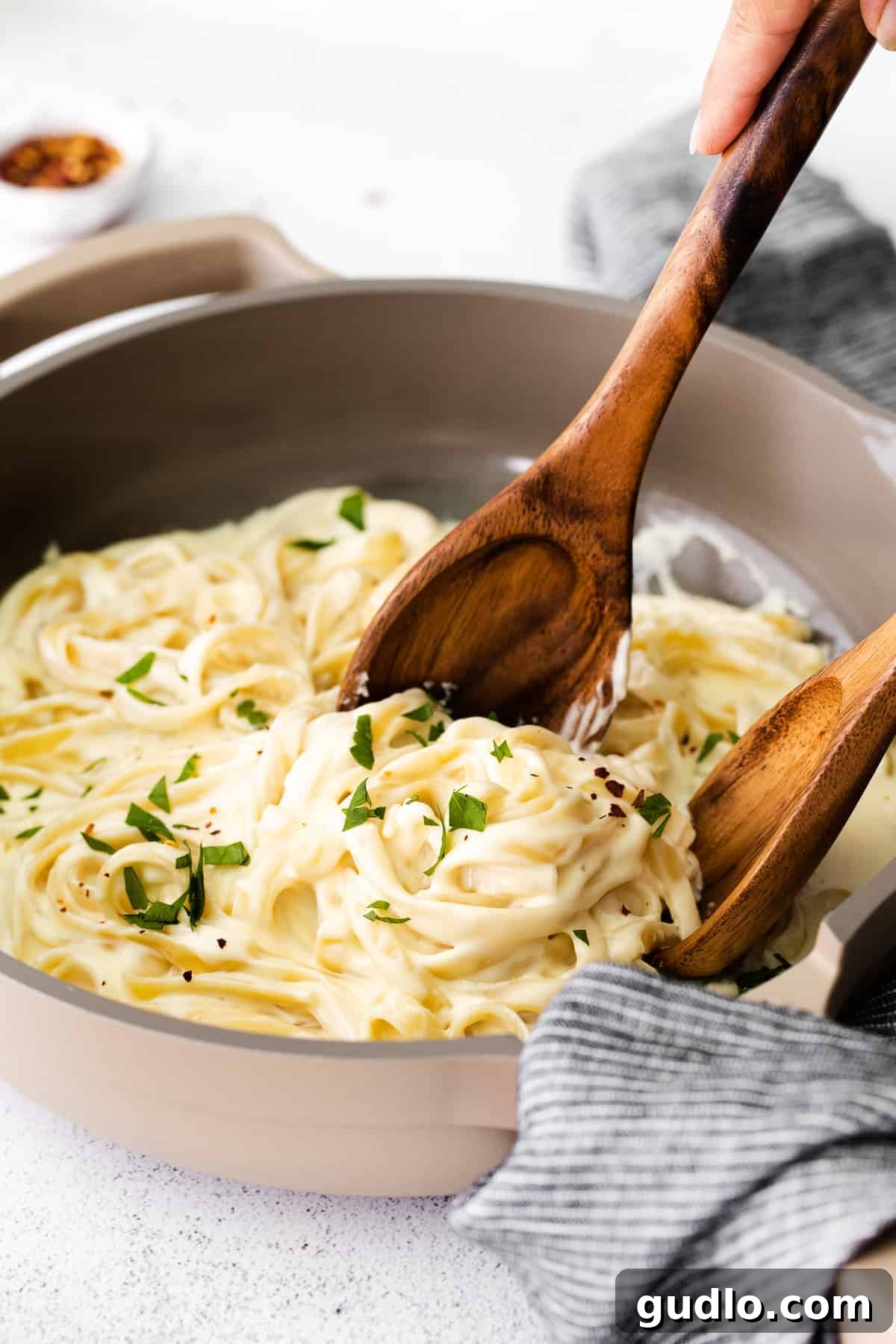 Experience the ultimate creaminess with our Alfredo Sauce featuring cream cheese, crafted with just 6 simple ingredients. An irresistible pairing for any pasta dish! Fettuccine pasta generously coated in thick, creamy cream cheese Alfredo sauce in a skillet, garnished with fresh parsley and ready to be served.