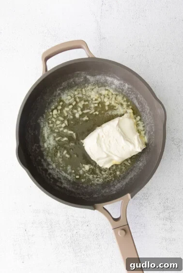 A frying pan with creamy alfredo sauce and a piece of cheese.