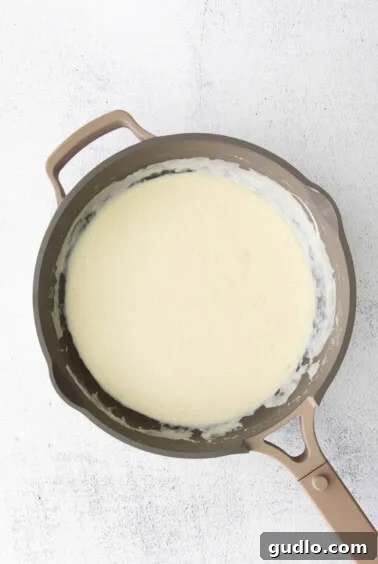 A frying pan with alfredo sauce and cream cheese blending together.