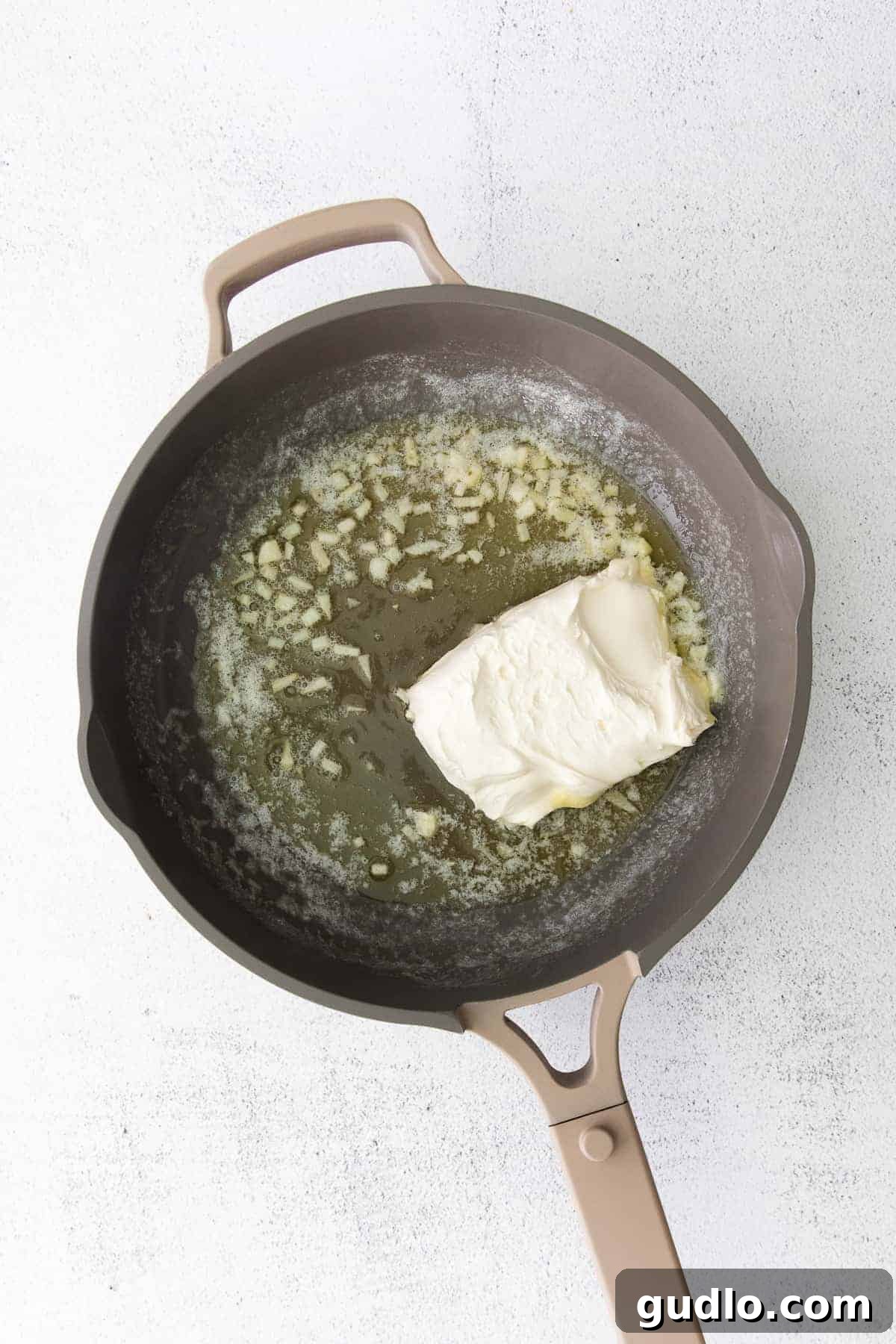 Watch the magic happen as butter, aromatic garlic, and softened cream cheese smoothly combine for a wonderfully creamy Alfredo base. Minced garlic and melted butter combined with softened cream cheese in a skillet, gently stirring to create the smooth, creamy base for Alfredo sauce.