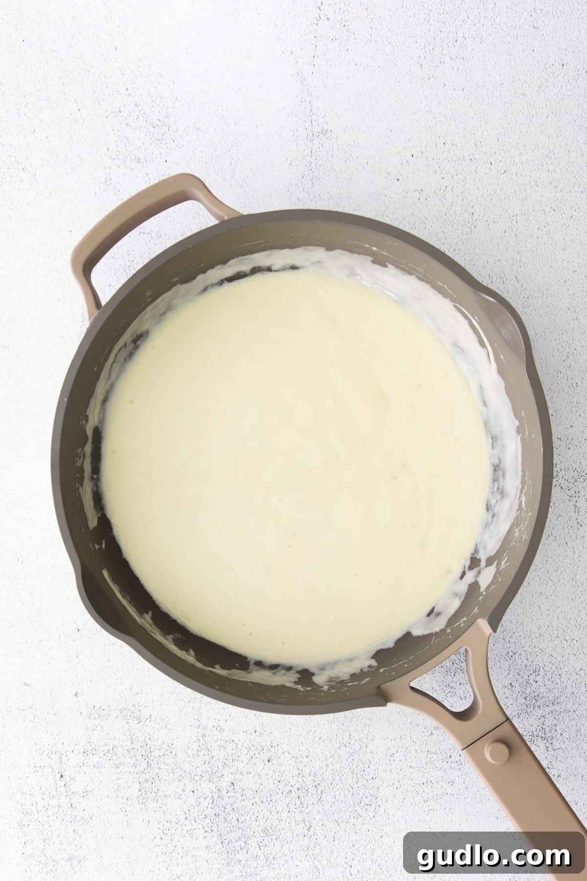 The perfect consistency: our creamy Alfredo sauce simmering to perfection, a testament to its effortless richness. Close-up of rich, creamy Alfredo sauce bubbling gently in a skillet, showcasing its smooth texture and appetizing sheen, ready to be tossed with pasta.