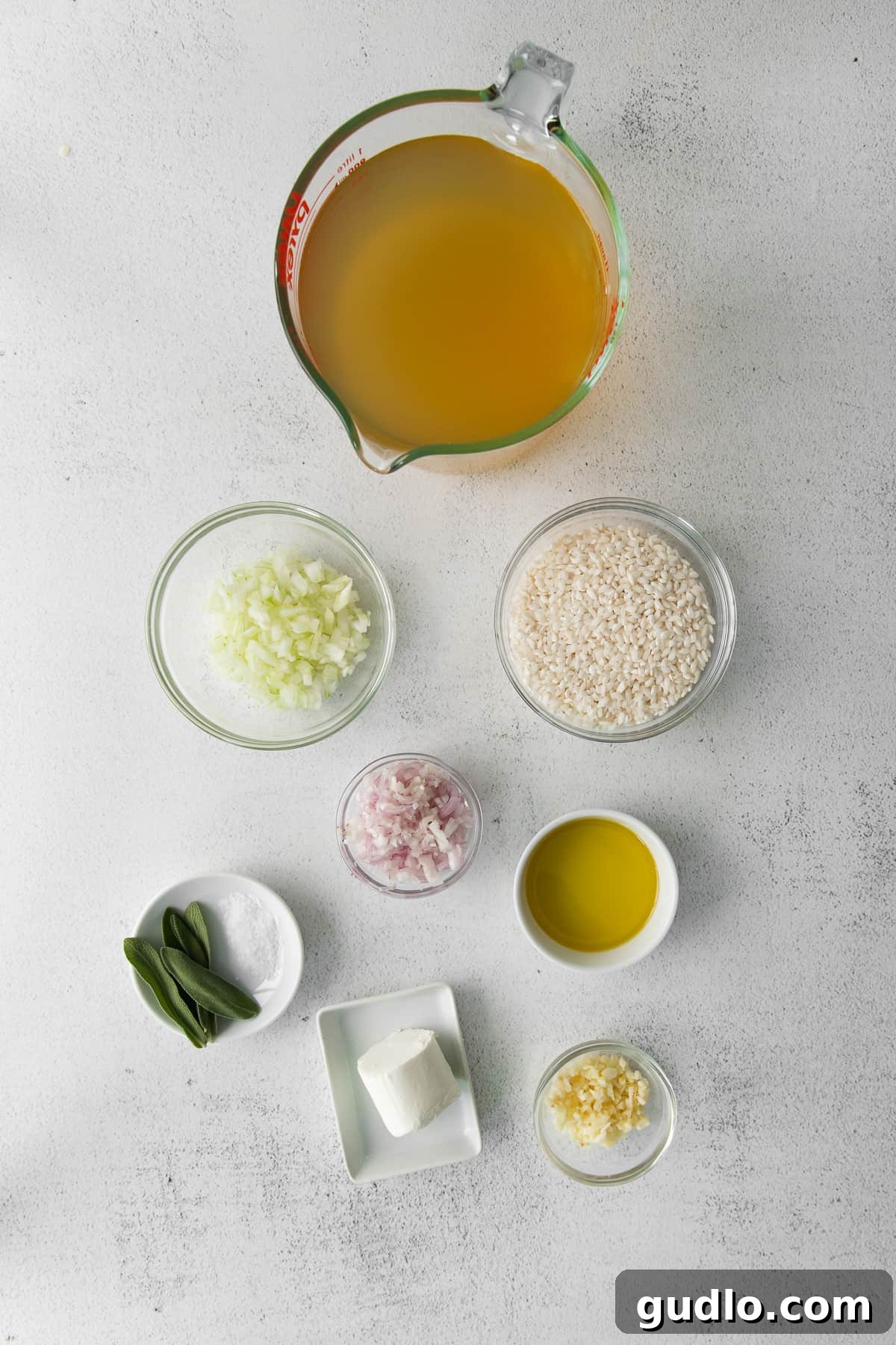 Fresh ingredients ready for your homemade goat cheese risotto. Essential ingredients for goat cheese risotto laid out on a kitchen countertop, including fresh sage, garlic, onions, olive oil, arborio rice, and a block of goat cheese.
