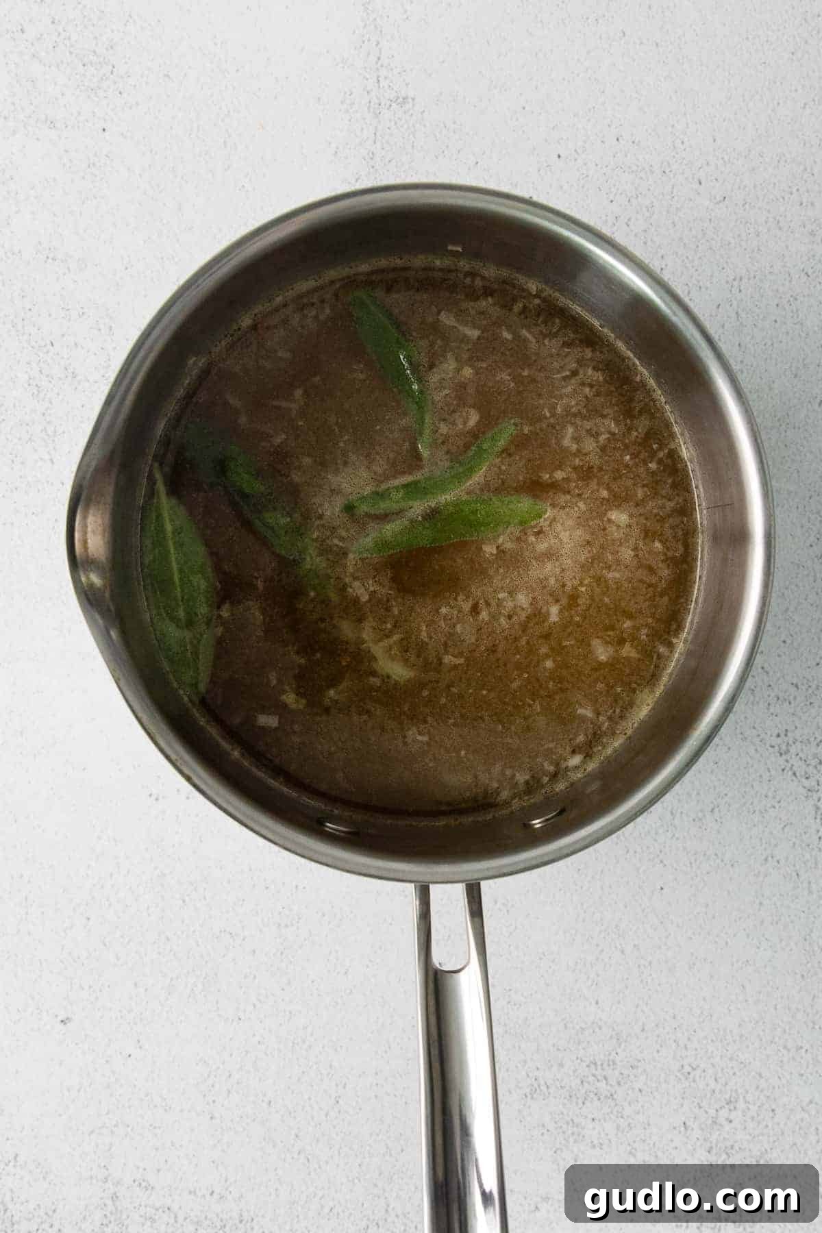 Aromatic broth infusing with sage, enhancing the depth of flavor for your risotto. A pot of simmering broth with fresh sage leaves, ready to be added to the risotto.