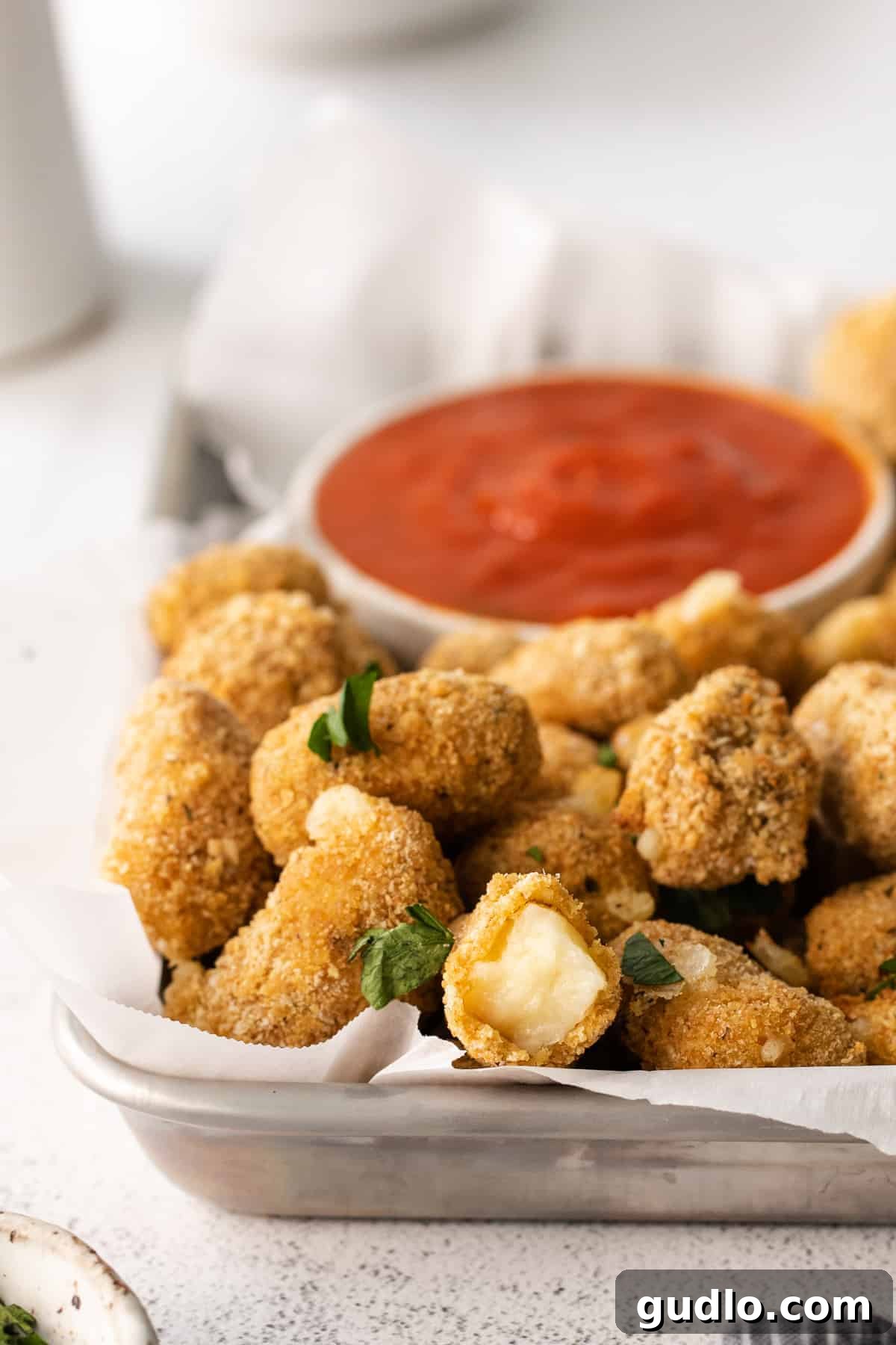 These air fryer cheese curds are made perfectly crispy in the air fryer in no time at all! Serve these as an appetizer or game day snack. air fryer cheese curds with a bowl of marinara sauce in the background