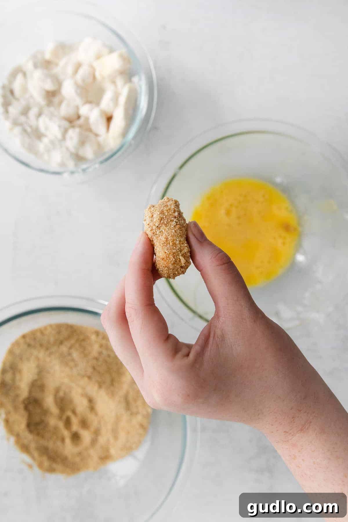 These air fryer cheese curds are made perfectly crispy in the air fryer in no time at all! Serve these as an appetizer or game day snack. cheese curd with breading about to be dipped into an egg wash