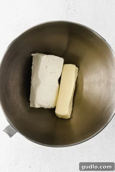 Velvety Chocolate Cream Cheese Delight 8 Softened cream cheese and butter creaming together in a metal mixing bowl, forming the smooth base for the frosting.