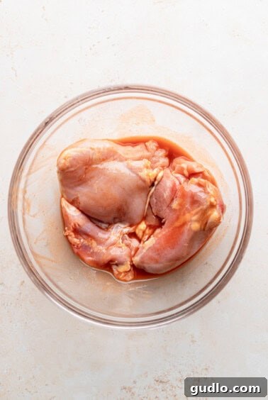 Chicken thighs marinating in a glass bowl.