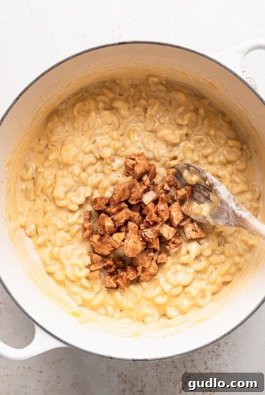 Macaroni and cheese with buffalo chicken in a white pot with a spoon.