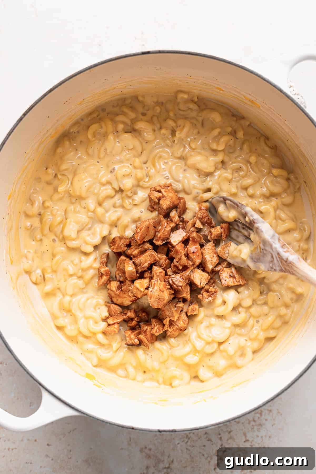 A vibrant, close-up shot of creamy macaroni and cheese generously topped with bright red, diced buffalo chicken, garnished with fresh green herbs, showcasing a perfect serving.