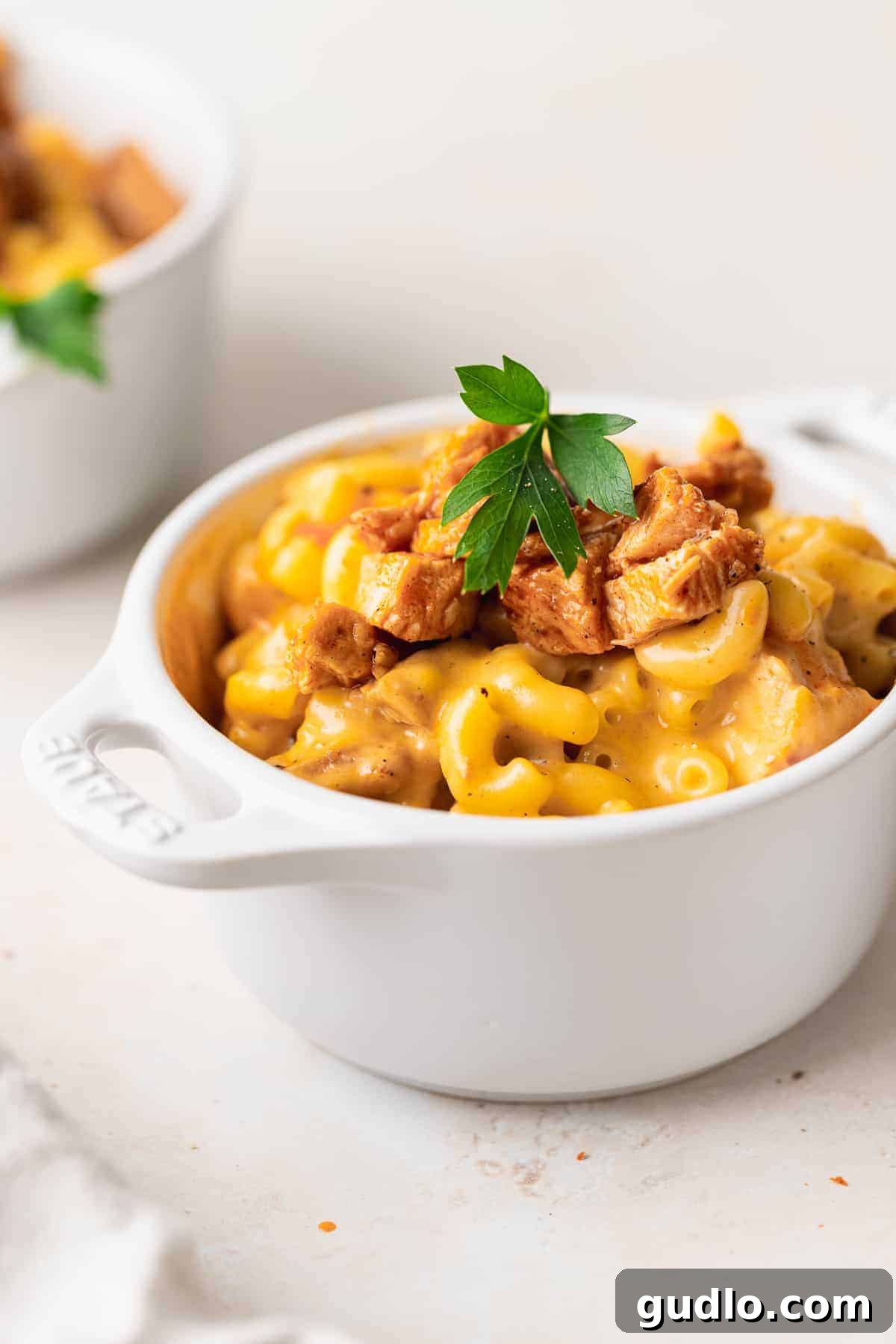 A close-up shot of a creamy, golden Buffalo Chicken Mac and Cheese, with visible macaroni noodles and tender chicken pieces, ready to be served in a rustic bowl.