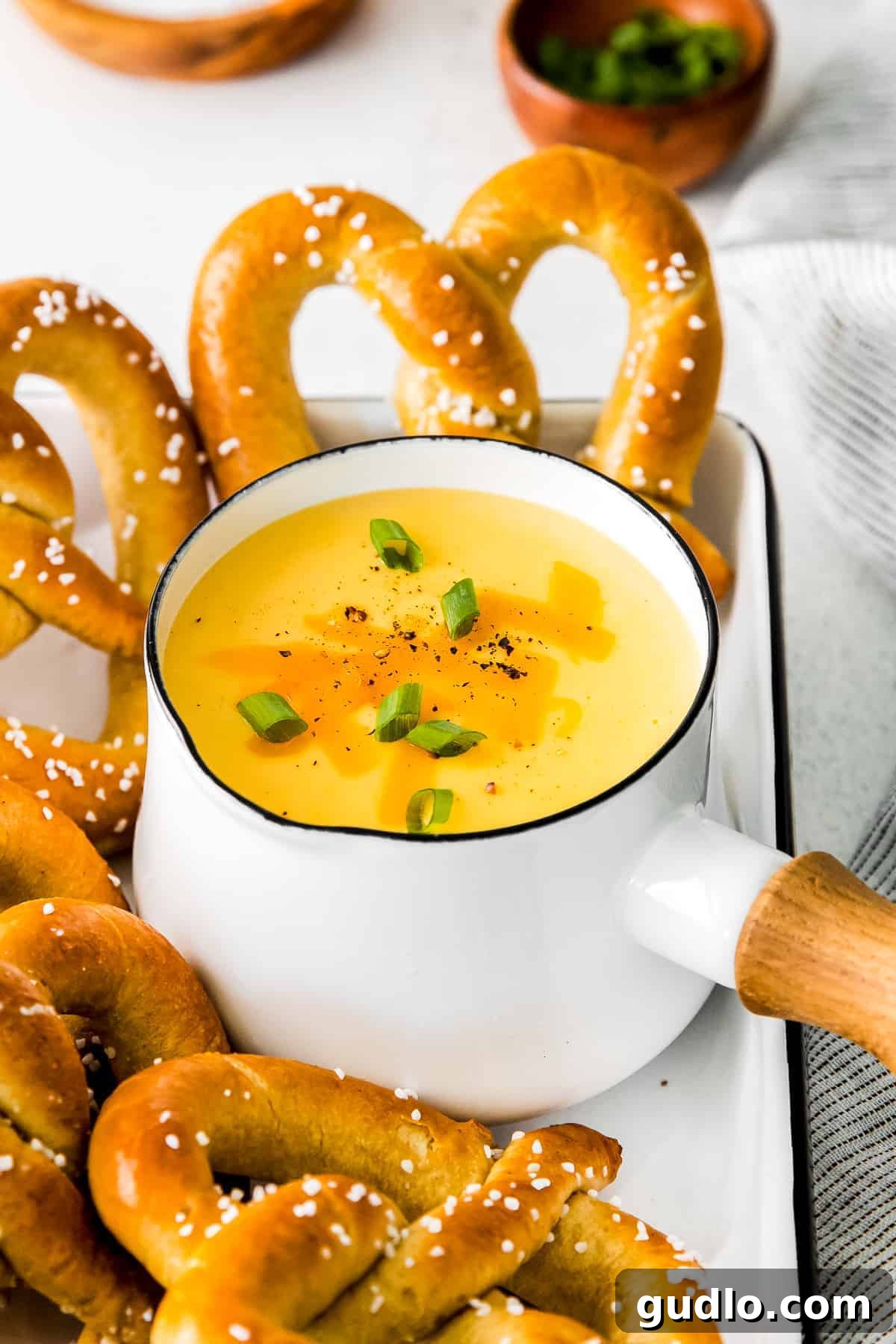Creamy Beer Cheese Fondue 3 A bubbling saucepan filled with golden beer cheese dip, surrounded by an assortment of soft pretzels, ready to be served at a party.
