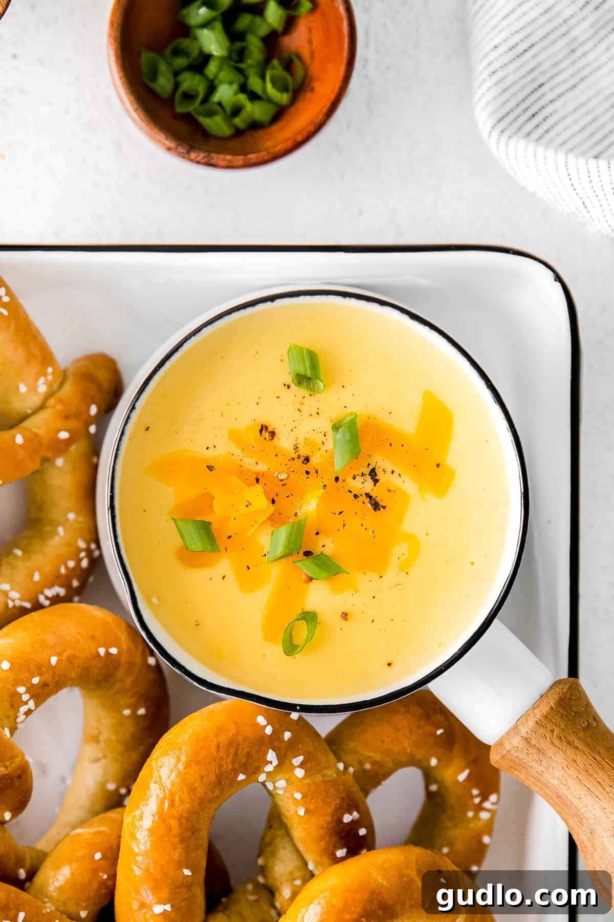Creamy Beer Cheese Fondue 7 A saucepan of creamy beer cheese dip, garnished with finely chopped green onions, ready for dipping various vegetables, crackers, and soft pretzels.