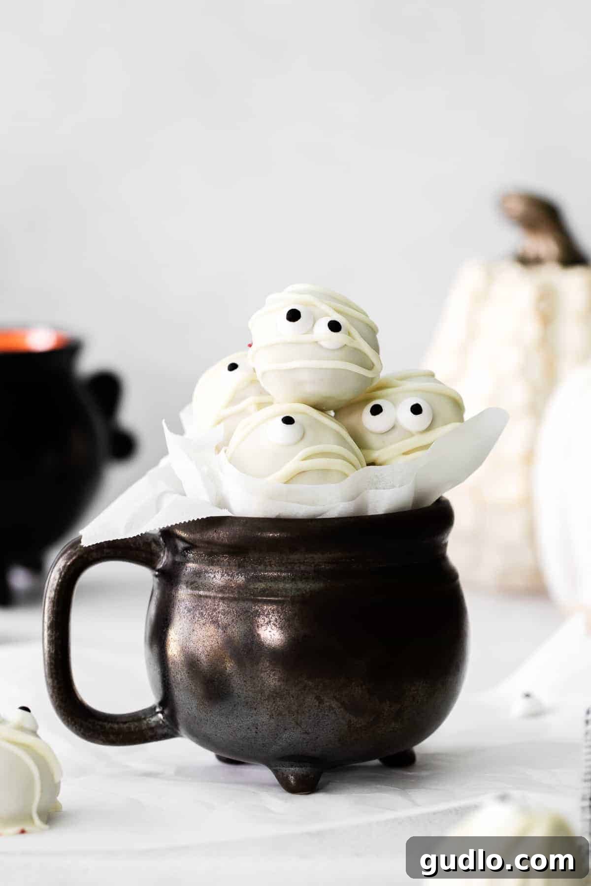 Make these spooky Red Velvet Mummy Truffles for a fun Halloween treat the whole family can help make! Adorable red velvet mummy truffles displayed in a festive cup, adorned with candy eyes and white chocolate bandages, ready for Halloween festivities.