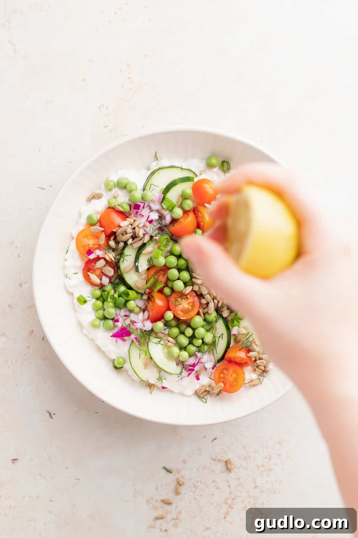 Finishing Cottage Cheese Salad with Lemon Juice A hand gently squeezing fresh lemon juice over the colorful cottage cheese salad, enhancing its freshness and flavor with a zesty finish.
