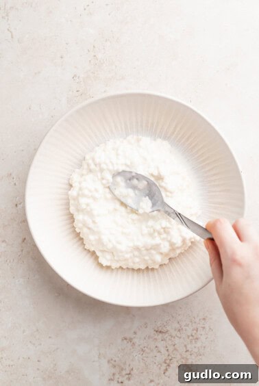 Wholesome Cottage Medley 3 A person's hand is holding a spoonful of cottage cheese salad in a white bowl.