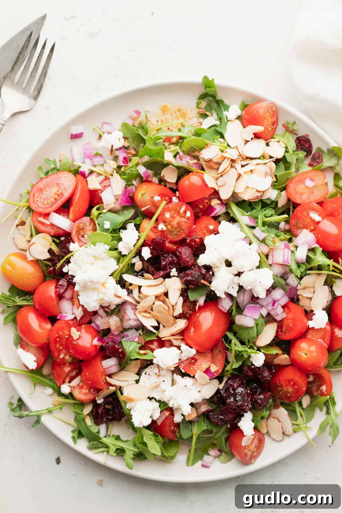 A beautifully plated arugula goat cheese salad, showcasing vibrant greens, creamy goat cheese crumbles, and red accents, ready to be enjoyed.