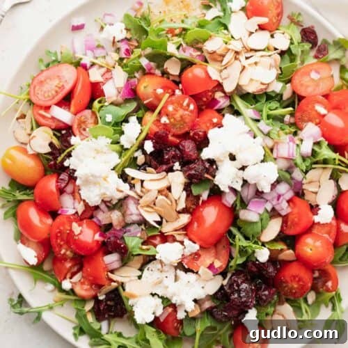 A plate of arugula salad with goat cheese, cranberries, and toasted almonds, looking fresh and appetizing.