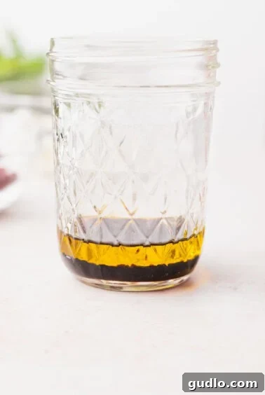Olive oil and balsamic vinegar are shown in a mason jar, alongside other salad ingredients, preparing for dressing.