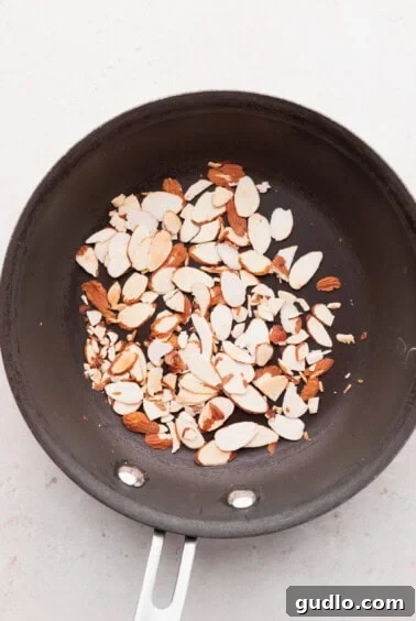 Slivered almonds are seen toasting in a small skillet on a stovetop, soon to be a crunchy addition to the salad.