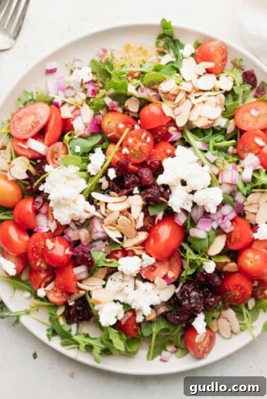 A vibrant plate of cranberry arugula salad, topped with crumbled goat cheese and slivered almonds, ready for serving.