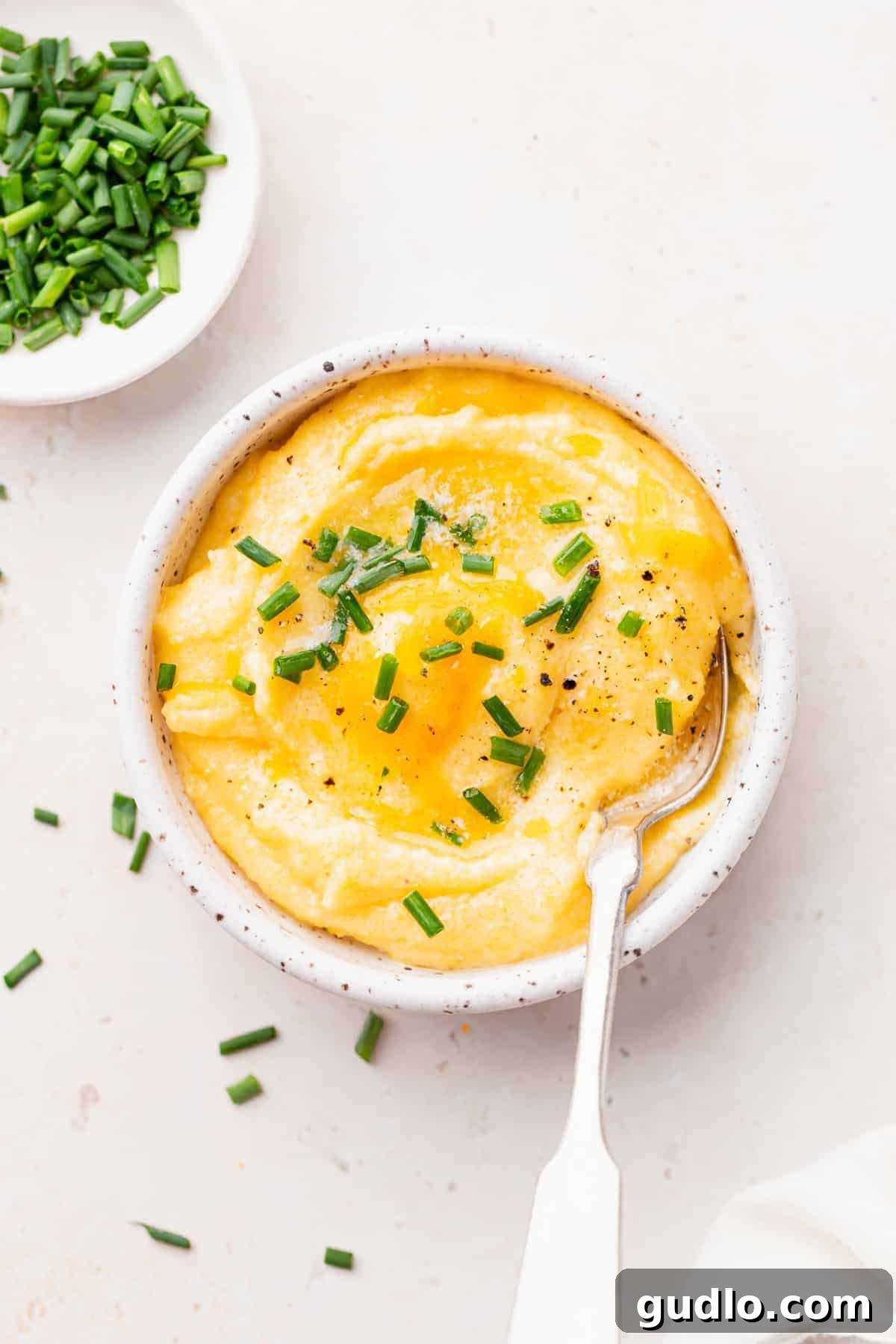 Creamy Cheese Grits: Ready to Enjoy A spoonful of luscious cheese grits, garnished with fresh chives, being lifted from a bowl, highlighting its creamy texture.