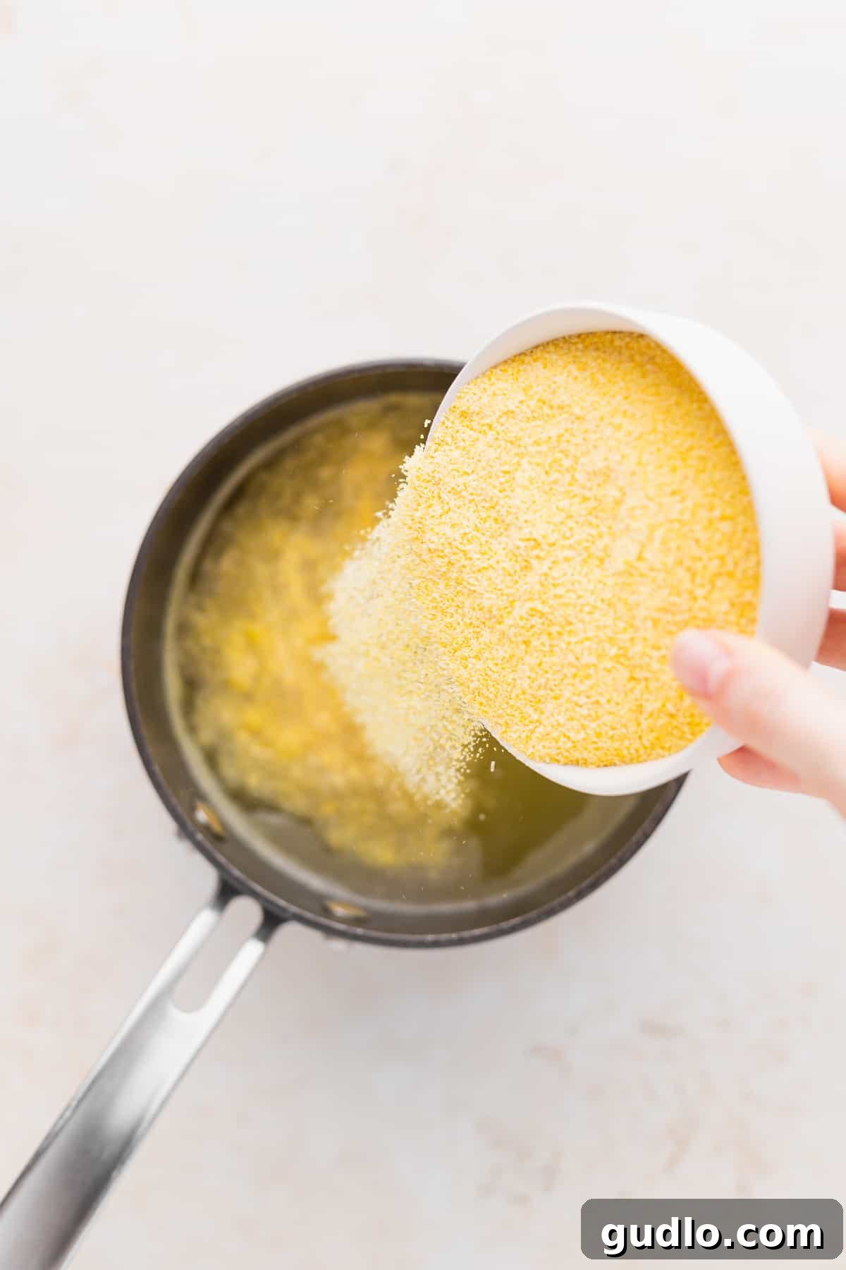 Adding Cornmeal to Broth for Perfect Grits Coarse ground cornmeal being carefully poured into simmering chicken broth, the first step to delicious cheese grits.