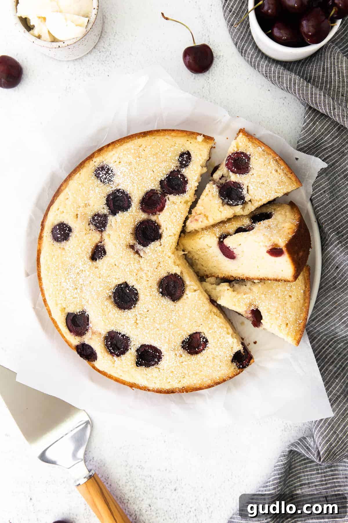 Velvety Cherry Ricotta Bliss 7 A cut Cherry Ricotta Cake, revealing its moist interior and scattered cherry pieces, topped with powdered sugar.