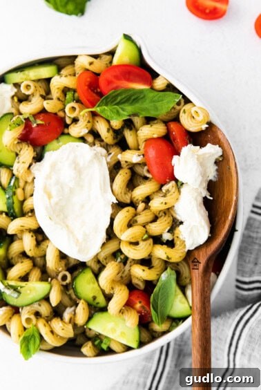 A flavorful bowl of pesto pasta salad with tomatoes, cucumbers, and creamy burrata, ready to be enjoyed.