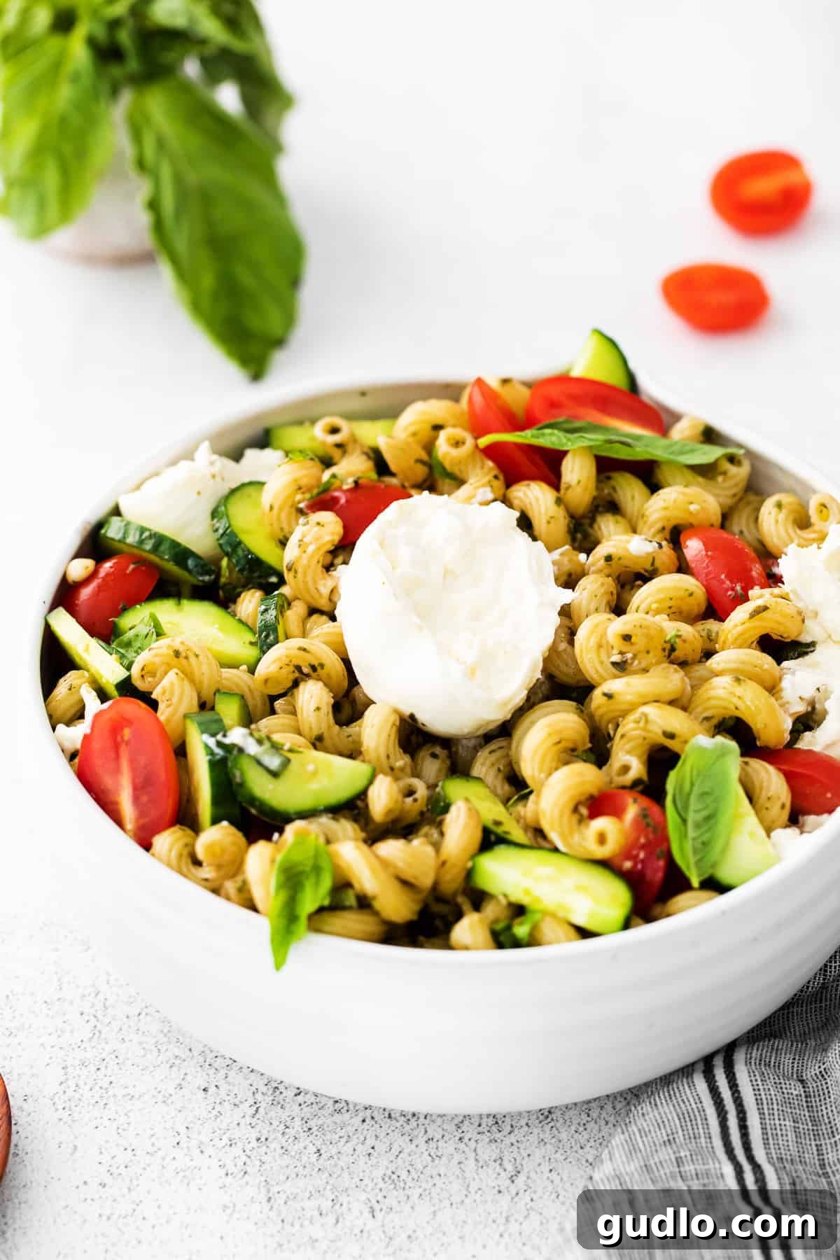 Creamy Burrata on Pesto Pasta Salad A close-up of a ball of burrata cheese delicately pulled apart into creamy chunks, nestled over a bed of vibrant pesto pasta salad.