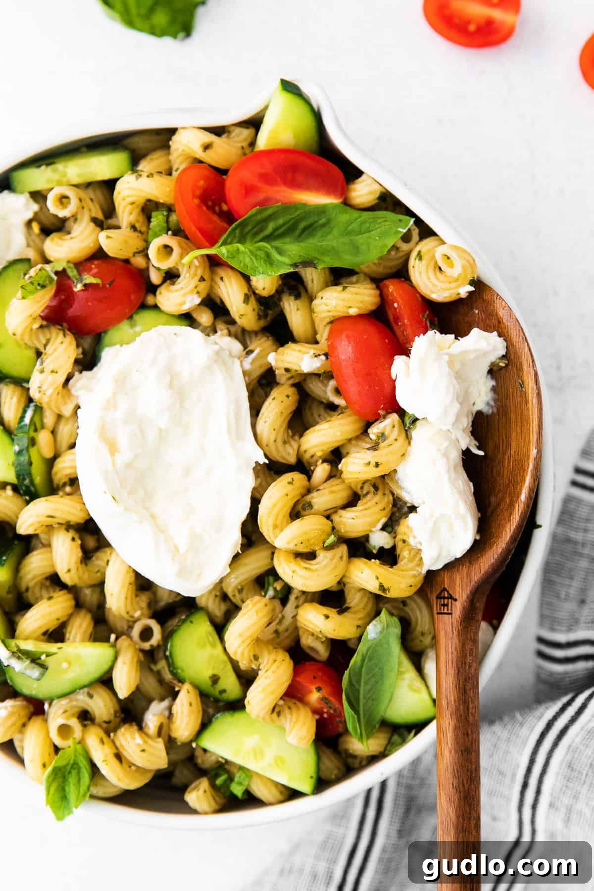 Serving the Perfect Pesto Pasta Salad A generous scoop of pesto pasta salad with burrata in a white bowl, ready to be served with a wooden spoon.