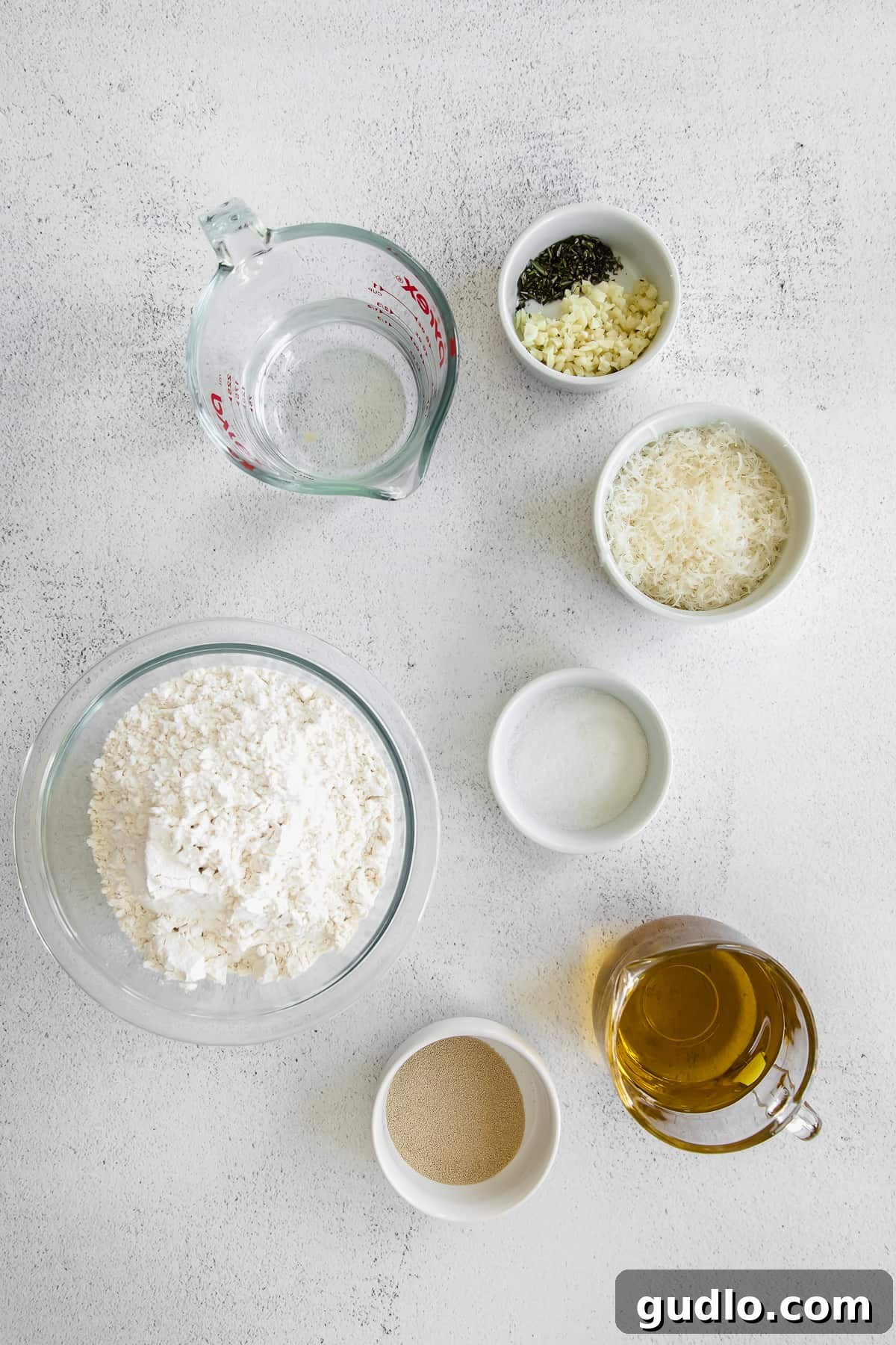 Focaccia Ingredients Display Essential ingredients for focaccia bread, including flour, olive oil, parmesan, and fresh rosemary, neatly arranged on a kitchen countertop