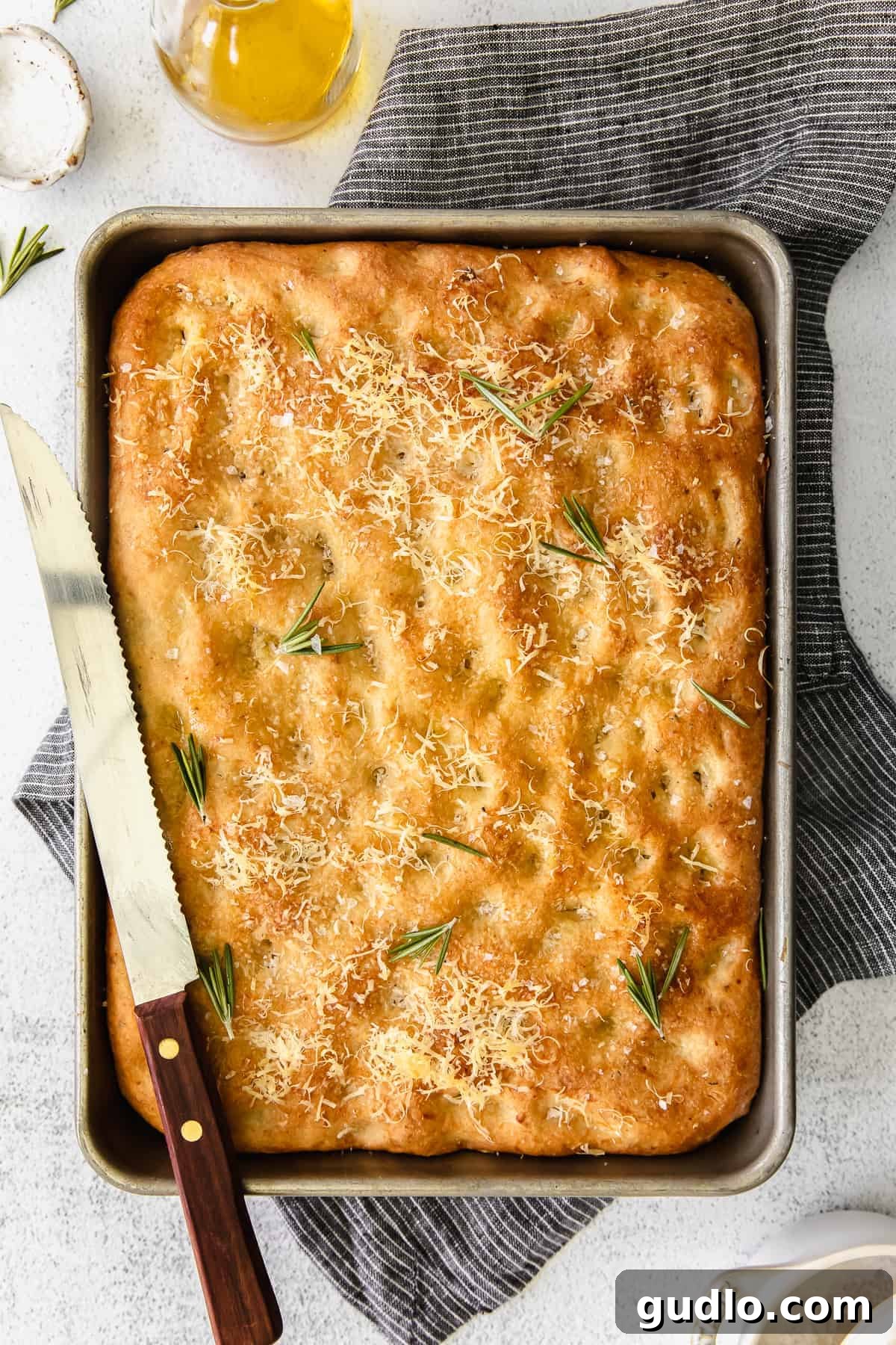 Ready-to-Serve Focaccia with Rosemary Delicious Parmesan Rosemary Focaccia bread, freshly baked and garnished with vibrant fresh rosemary sprigs on a rustic surface