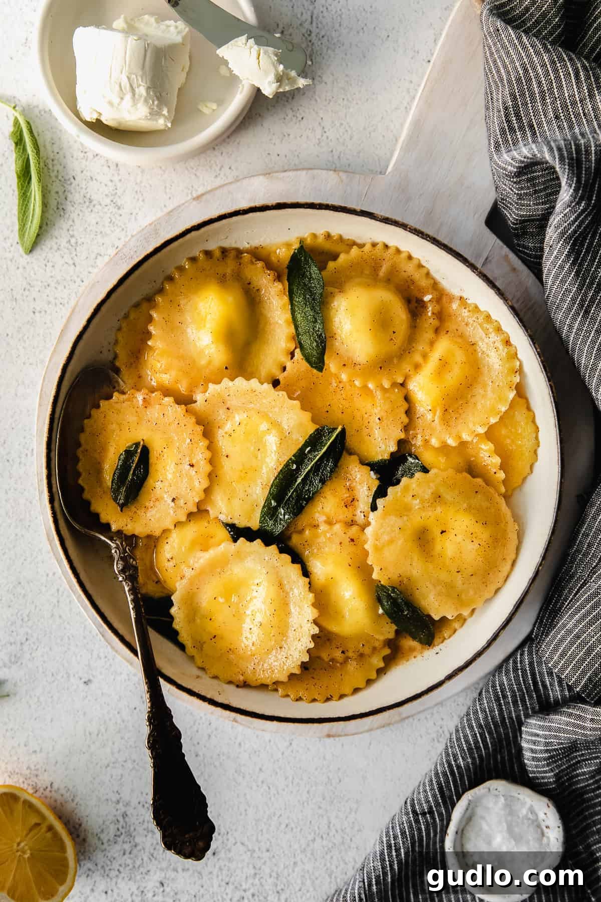 Homemade Goat Cheese Ravioli with Sage Brown Butter A bowl of freshly cooked goat cheese ravioli topped with fragrant sage leaves and a drizzle of brown butter sauce, ready to be enjoyed.