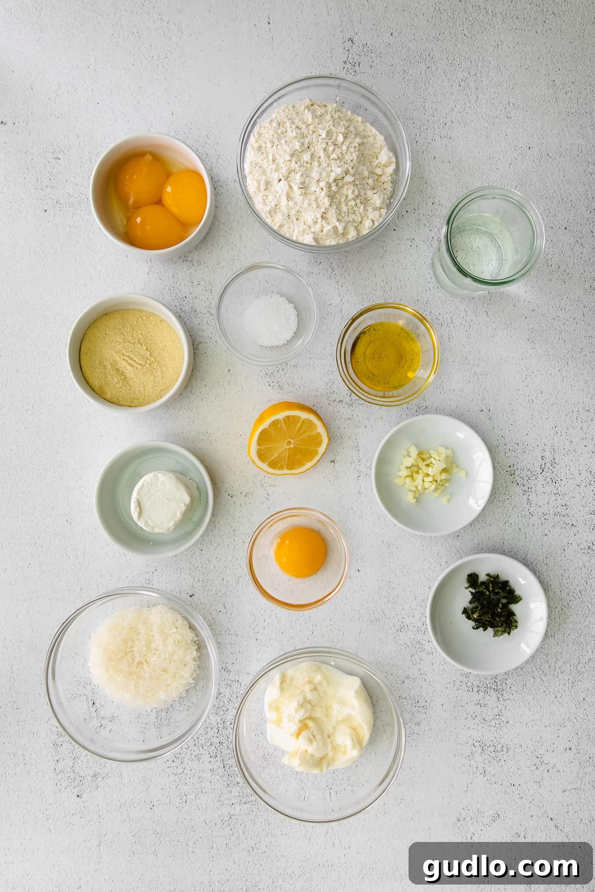 Goat Cheese Ravioli Ingredients Display Various ingredients for goat cheese ravioli, including flours, eggs, cheeses, and herbs, neatly arranged in separate bowls on a wooden surface.