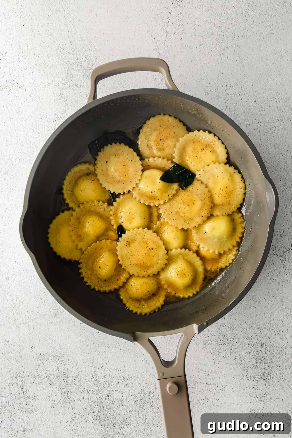 Goat Cheese Ravioli in Brown Butter Sauce Freshly cooked goat cheese ravioli tossed in a rich brown butter sauce with sage leaves, simmering in a frying pan.