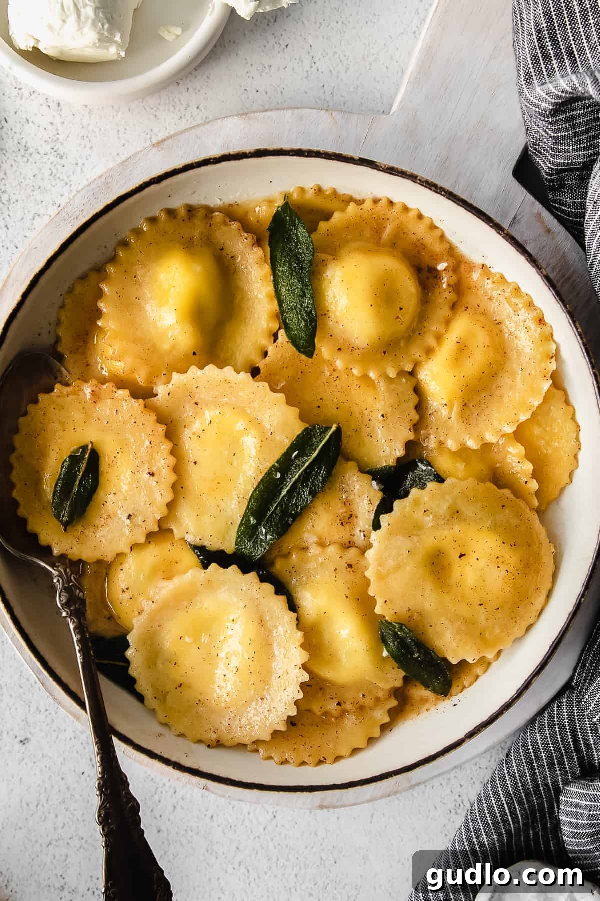 Goat Cheese Ravioli Served A serving of goat cheese ravioli in a white bowl, garnished with fresh sage, depicting a perfect gourmet meal.