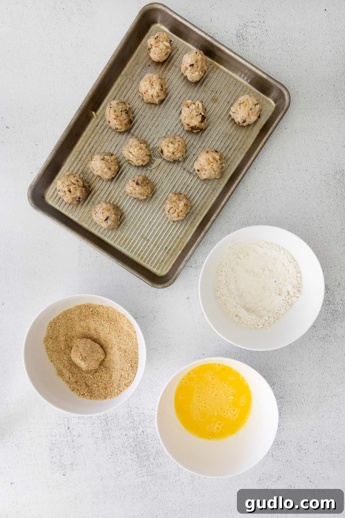 Got leftover risotto? Make Parmesan Arancini - a delicious fried rice ball appetizer! Hands carefully dipping a rice ball into a bowl of breadcrumbs as part of the breading process.