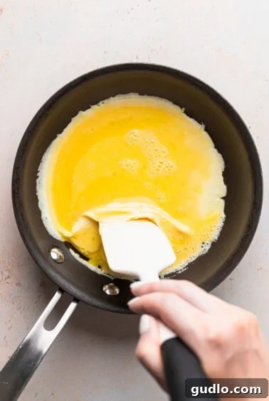A person making a cheese omelette with a spatula in a frying pan, demonstrating the initial stage of folding.