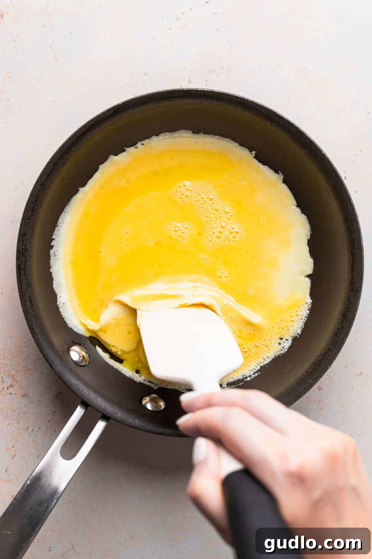 The initial stage of cooking a cheese omelette in a nonstick skillet, with a spatula gently folding the edges to allow uncooked egg to flow underneath.
