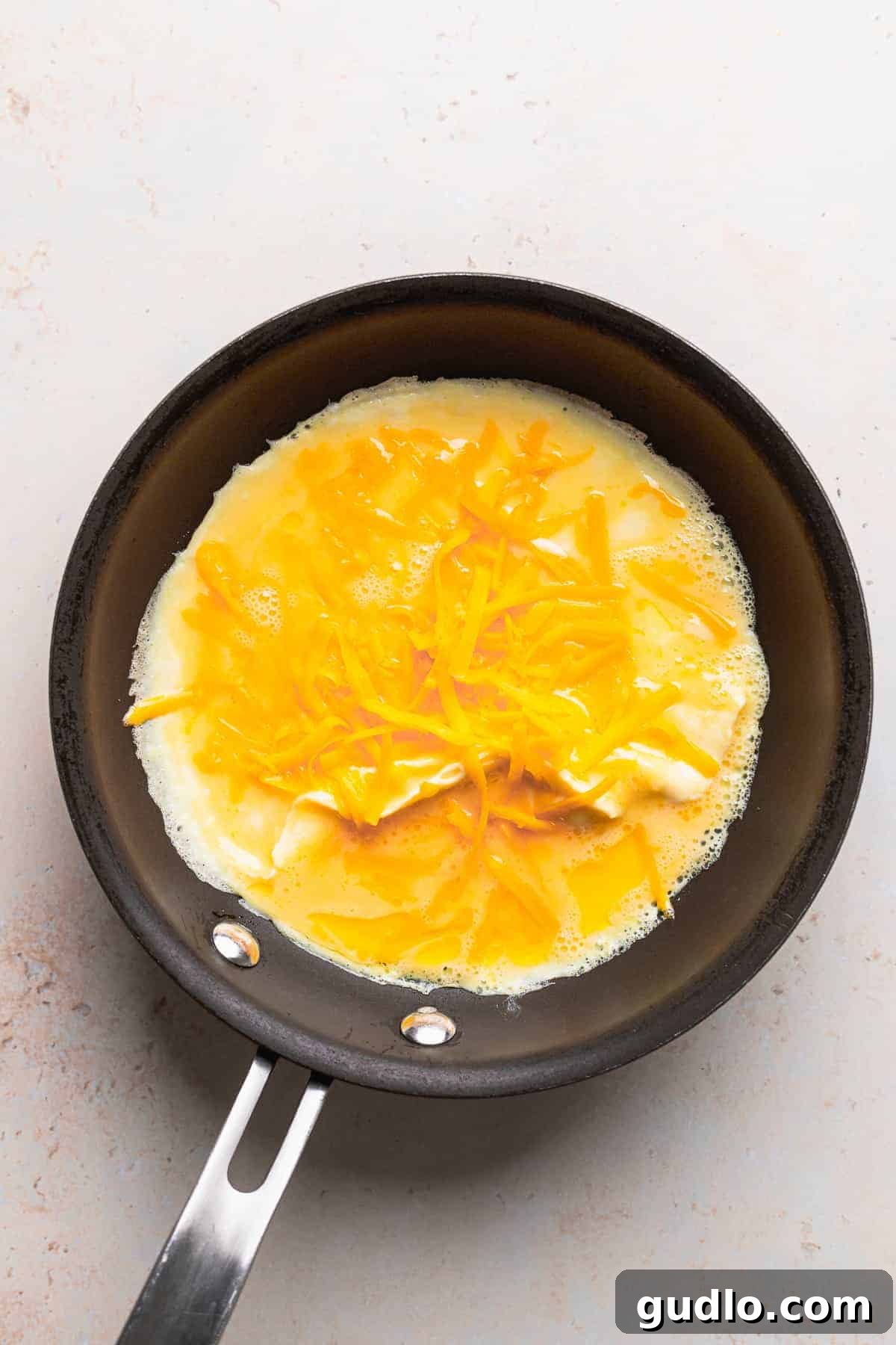 A vibrant cheese omelette cooking in a nonstick skillet, topped with a generous sprinkle of shredded cheddar cheese, melting into the eggs.