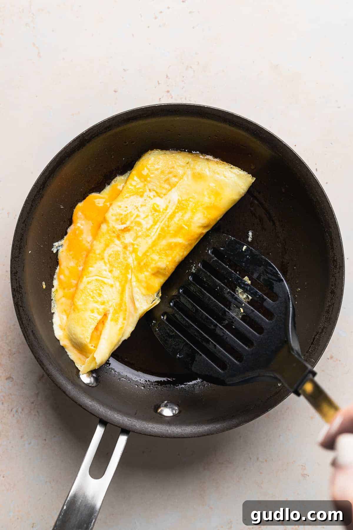 A skilled hand using a spatula to gently fold a cooking cheese omelette in a nonstick skillet, preparing it for plating.