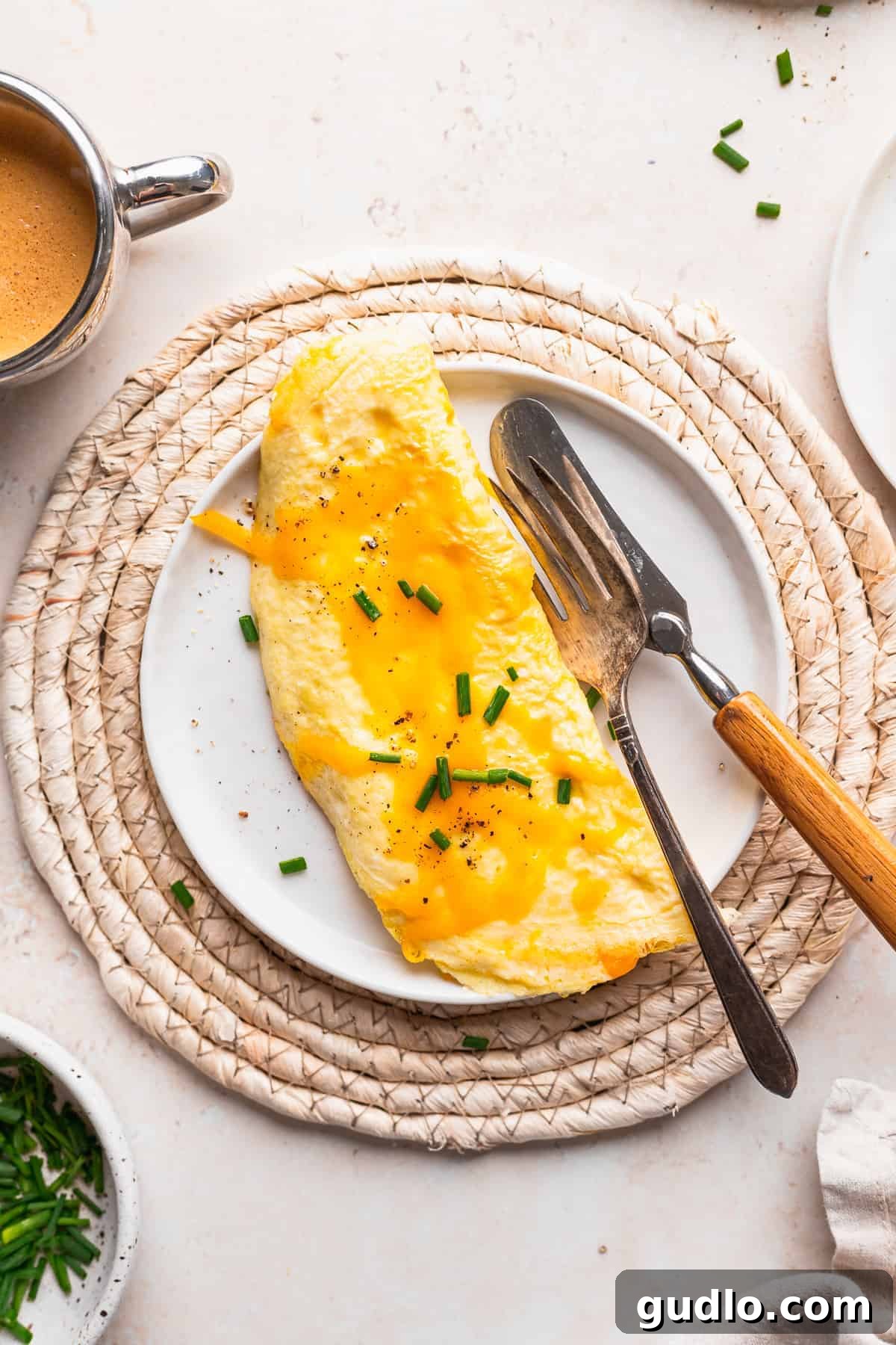 A freshly cooked cheese omelette elegantly presented on a white plate, garnished with a sprinkle of fresh green chives, highlighting its fluffy texture.