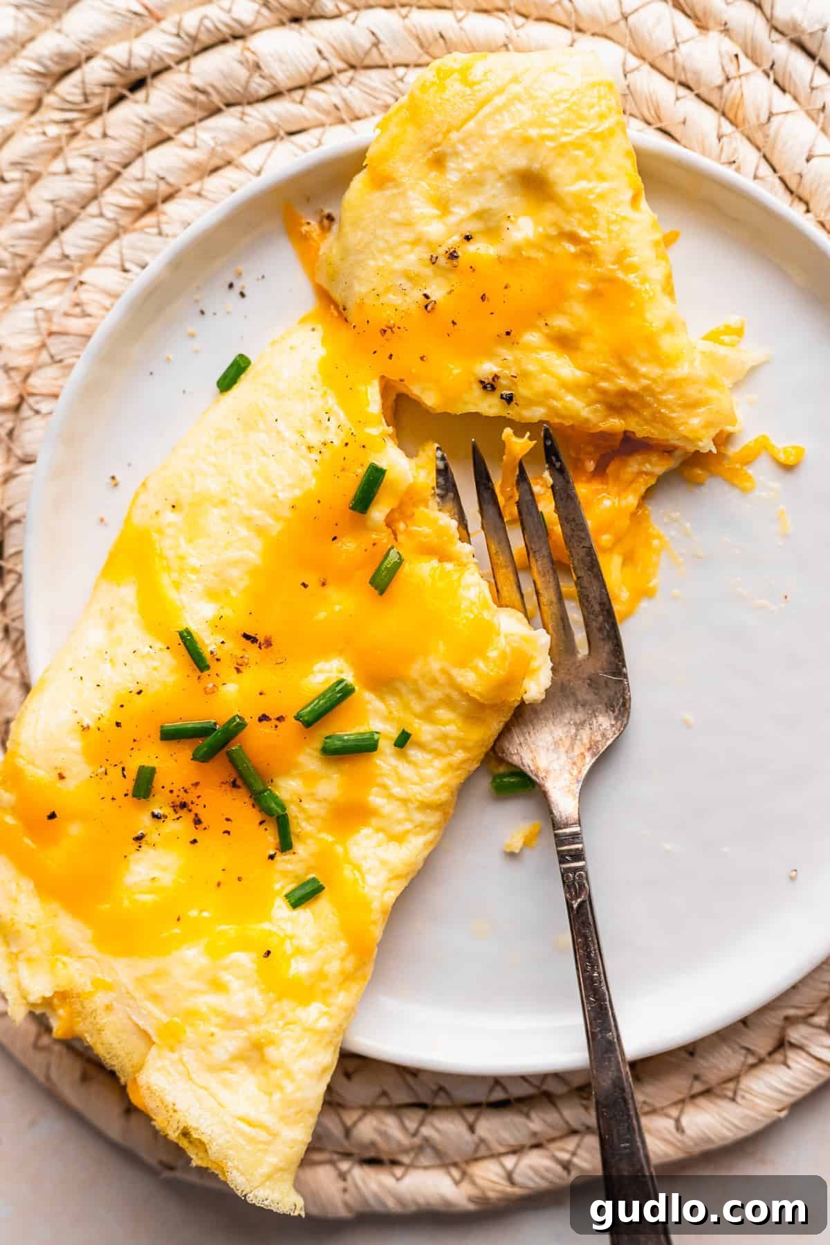 A delicious cheese omelette on a plate, being gently cut open with a fork to reveal its fluffy interior and melted cheese.