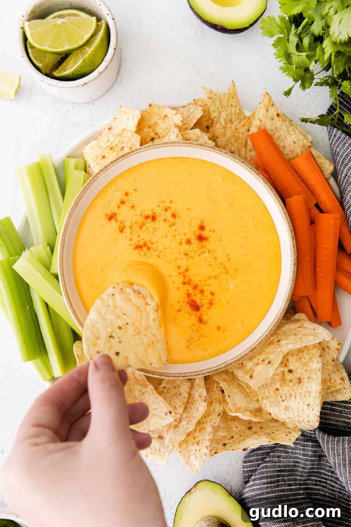 Creamy homemade nacho cheese sauce in a bowl, surrounded by crispy tortilla chips, vibrant carrot sticks, and fresh celery for dipping.