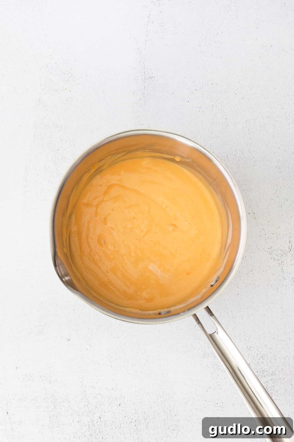 Nacho cheese sauce simmering in a saucepan, being whisked to a smooth, creamy consistency on the stovetop.